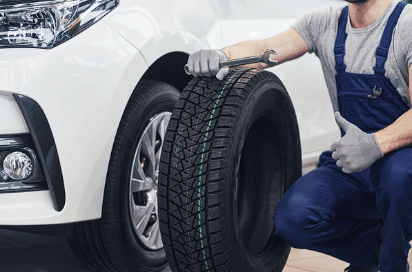 An auto mechanic replacing a worn tire with used car parts
